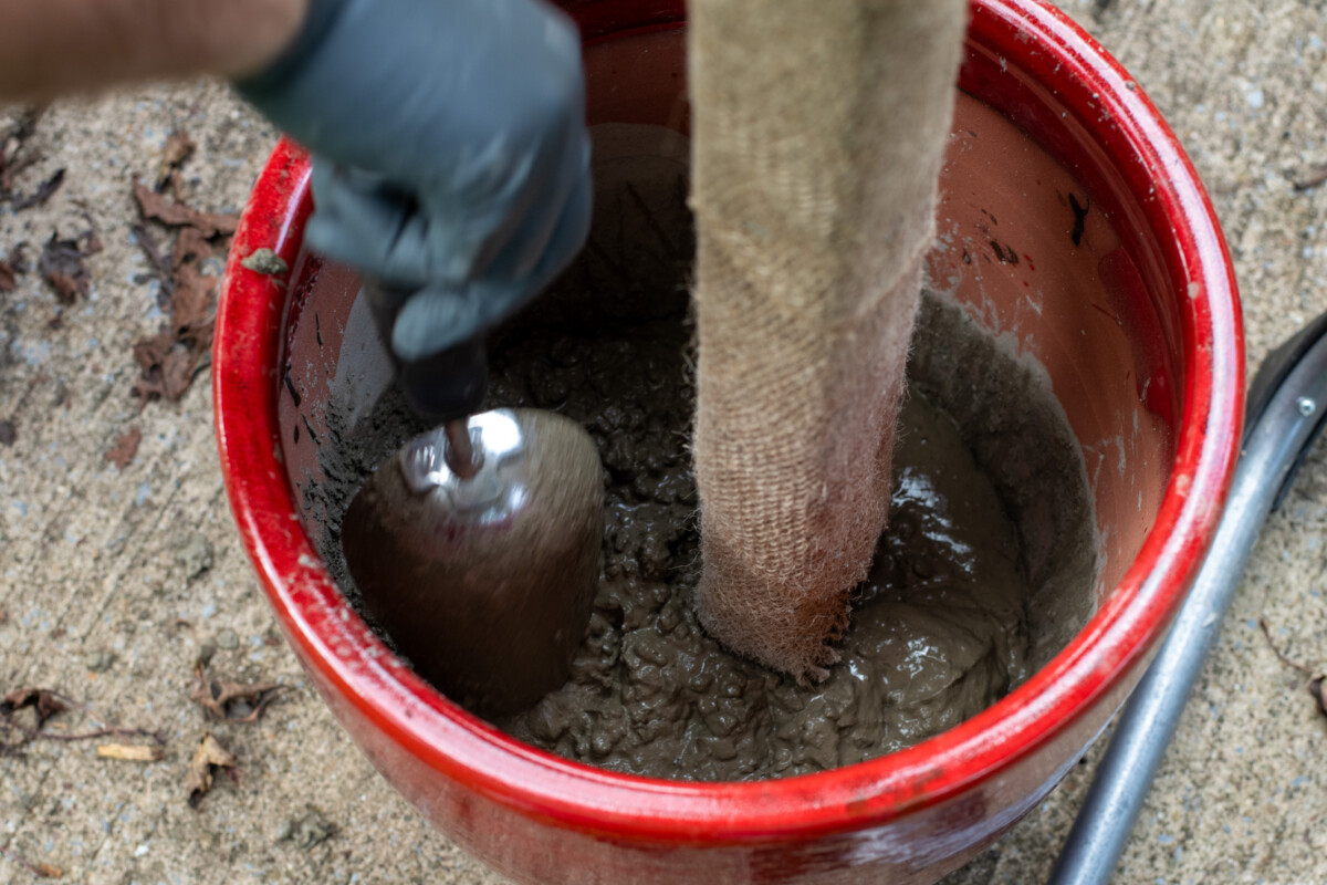 Man's hand shown using a trowel to settle concrete in bottom of planter